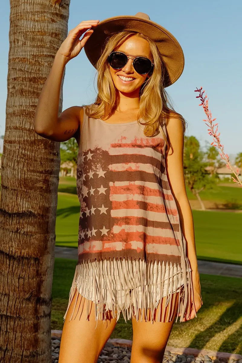 Woman wearing American flag fringe tank top with fringe hem, sunglasses, and hat, enjoying summer outdoors.