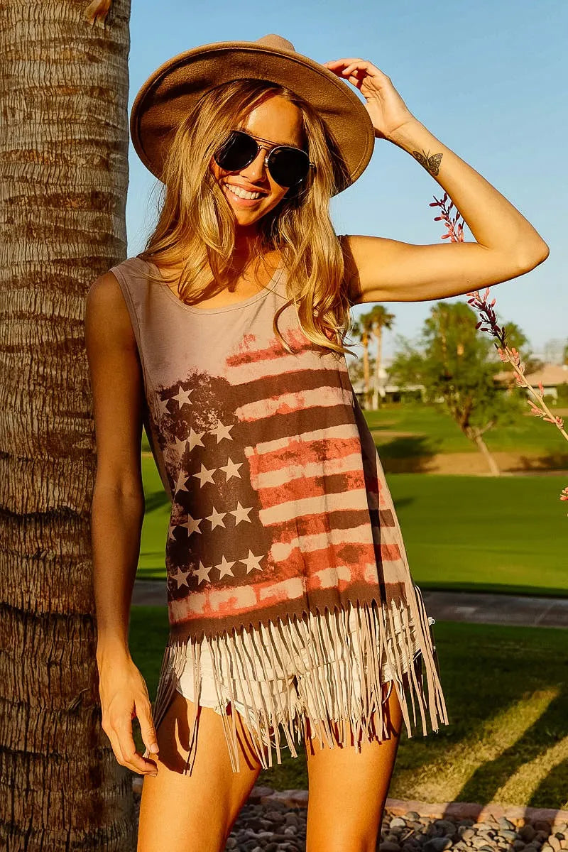 Woman wearing an American flag fringe tank top, sunglasses, and hat, enjoying summer outdoors.